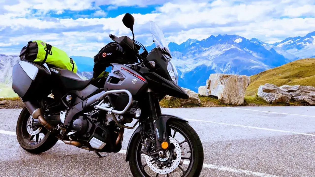 Szary motocykl Suzuki V-Strom, idealny motocykl do turystyki we dwoje, zaparkowany na tle majestatycznych gór i błękitnego nieba.