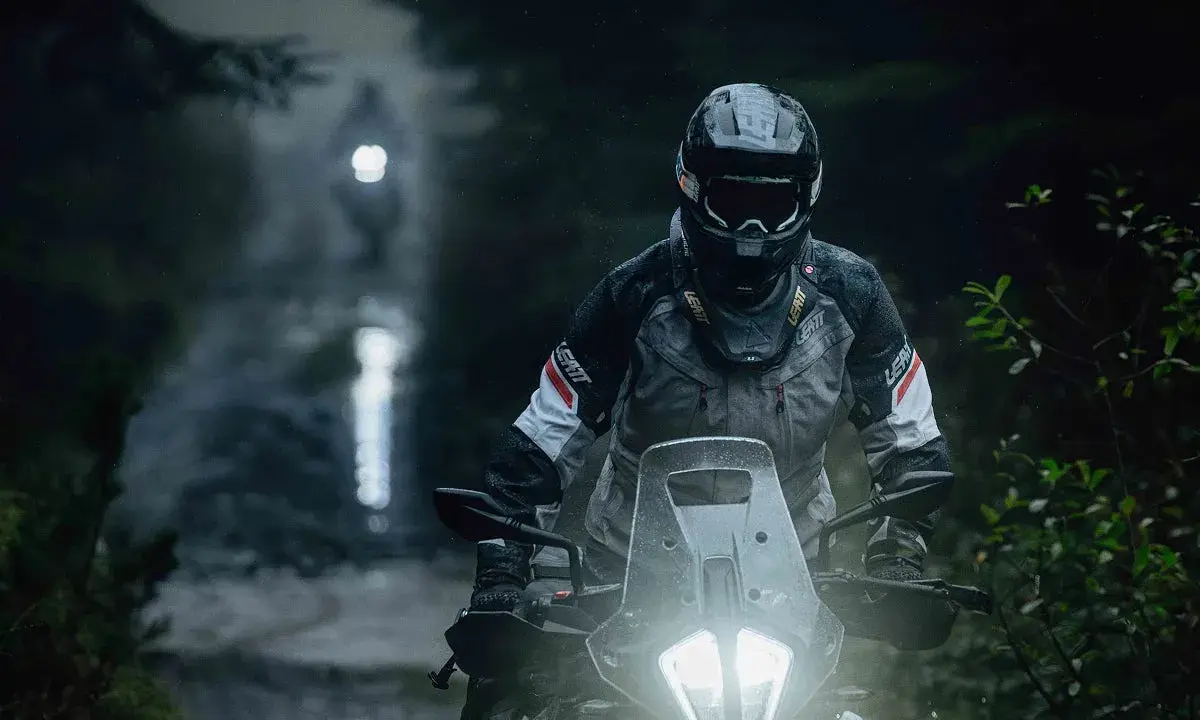 Motocyklista w kasku i kurtce Leatt przemierza leśną drogę w deszczu. Jazda na motocyklu w trudnych warunkach.
