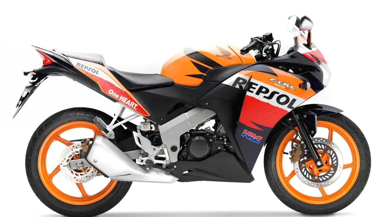Pomarańczowo-czarny motocykl Honda CBR 125R w barwach Repsol, gotowy do jazdy z mocą V-max.
