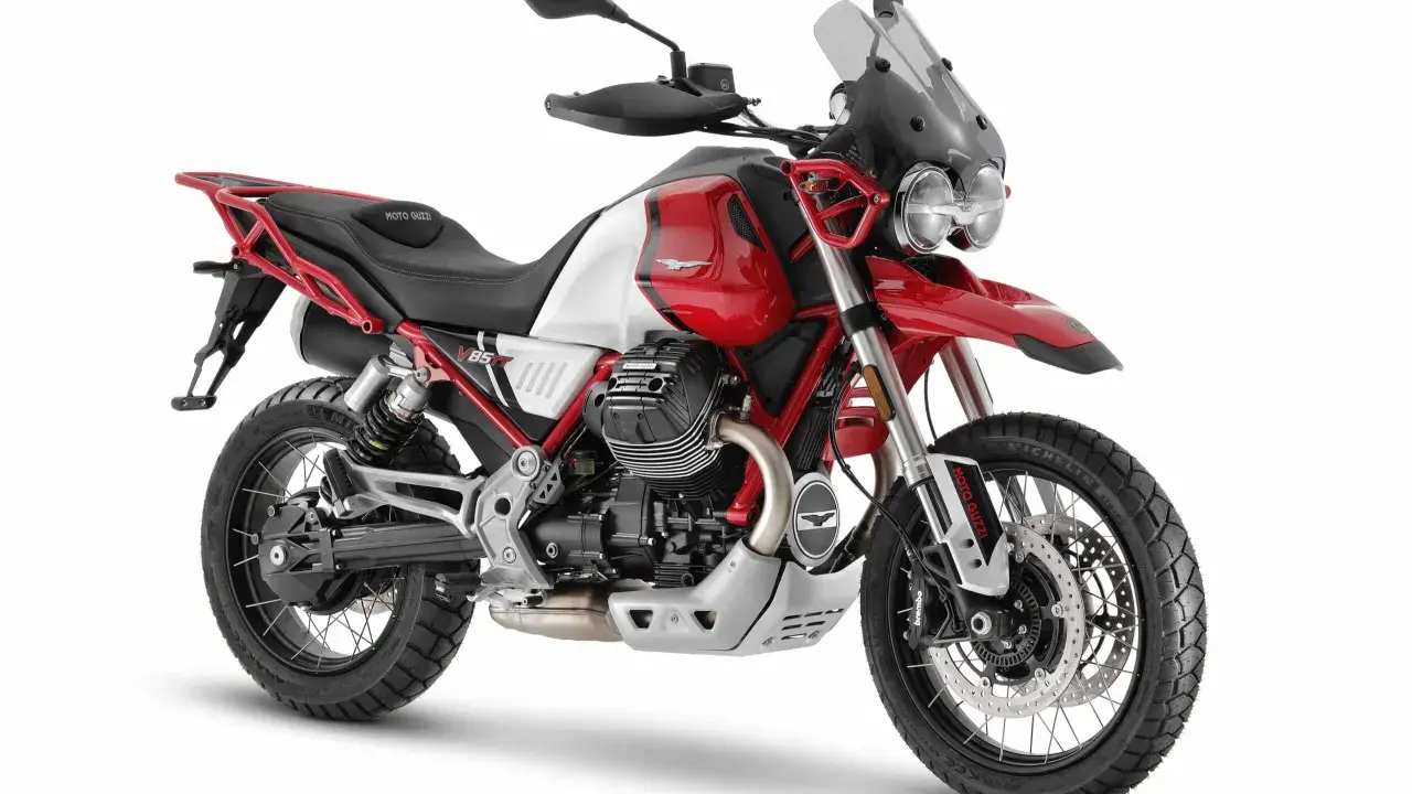 Czerwono-biały motocykl Moto Guzzi V85 TT z czarnym siedzeniem i akcentami, gotowy na przygodę.