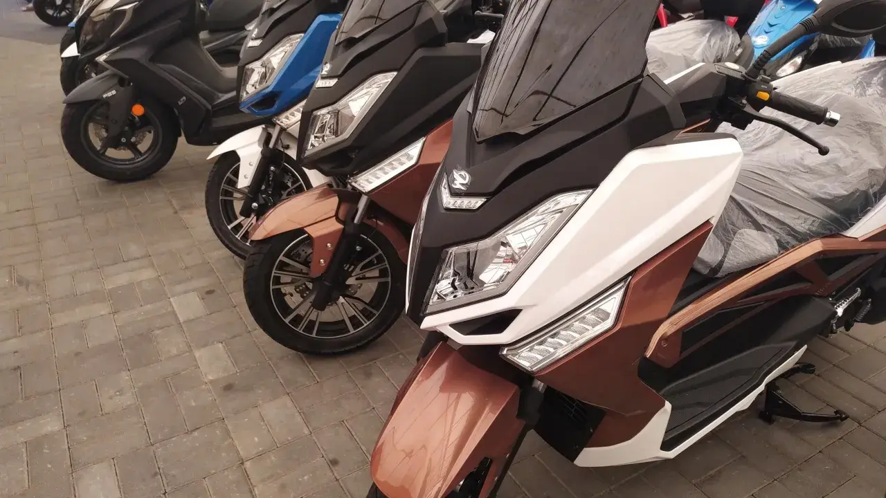 Kilka skuterów, w tym brązowy zipp qr max 125, stoi na chodniku.