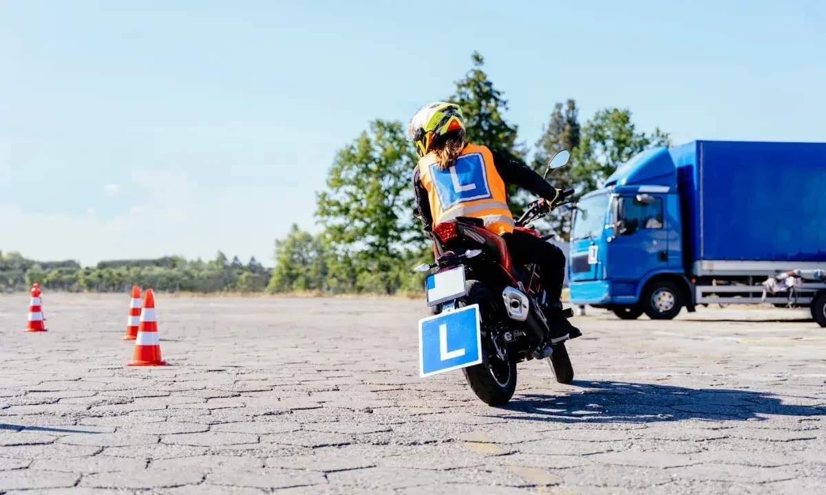 Osoba na motocyklu z literą "L" na kamizelce i tablicy, ćwiczy jazdę. Mam prawo jazdy B, chcę zrobić A.