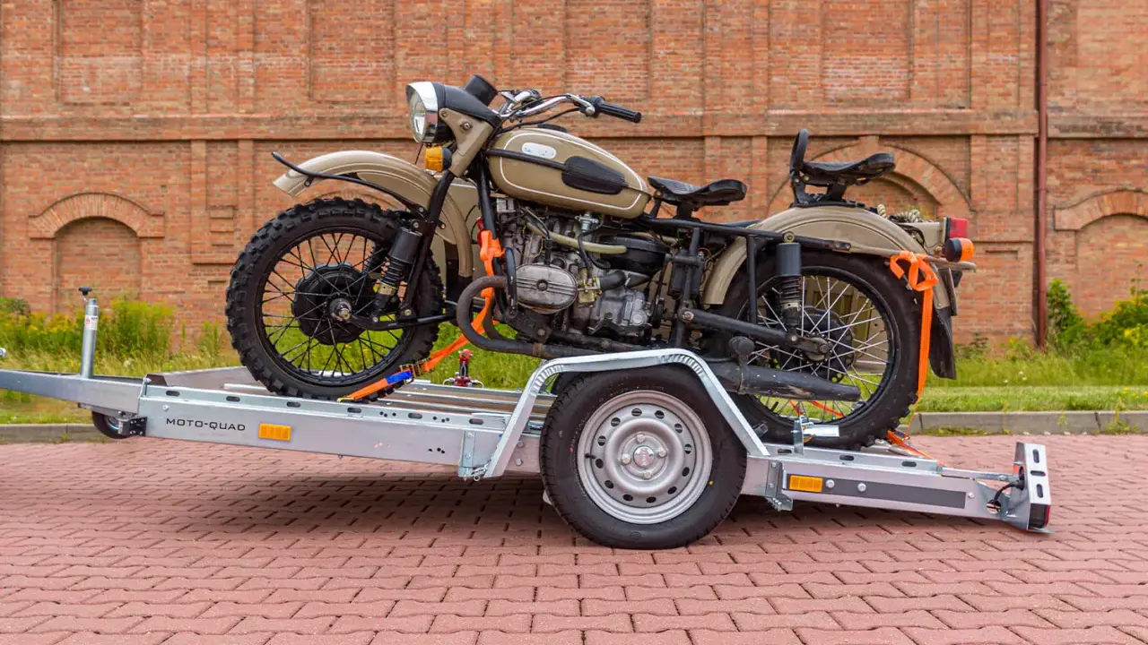 Motocykl Ural zabezpieczony pasami na przyczepie, pokazujący, jak przewieźć motocykl na zwykłej przyczepie.