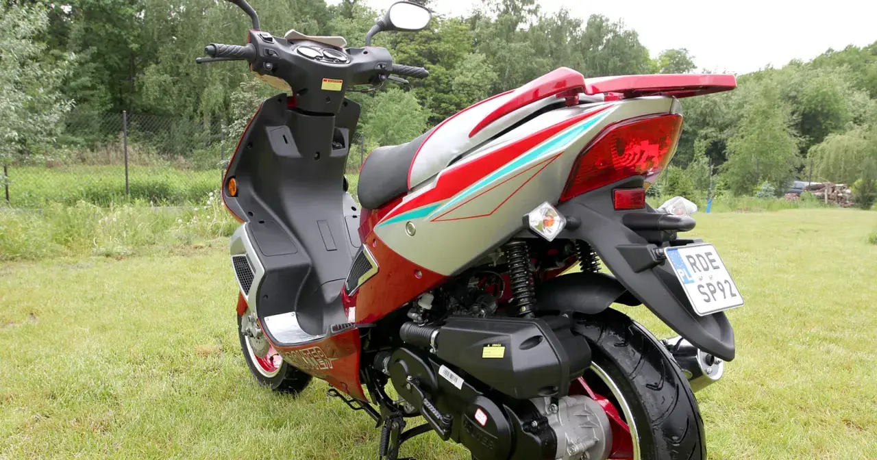 Czerwony skuter 50cc na trawie. Zastanawiasz się, ile jedzie skuter 50 bez blokad? Ten model wygląda na gotowy do szybkiej jazdy!