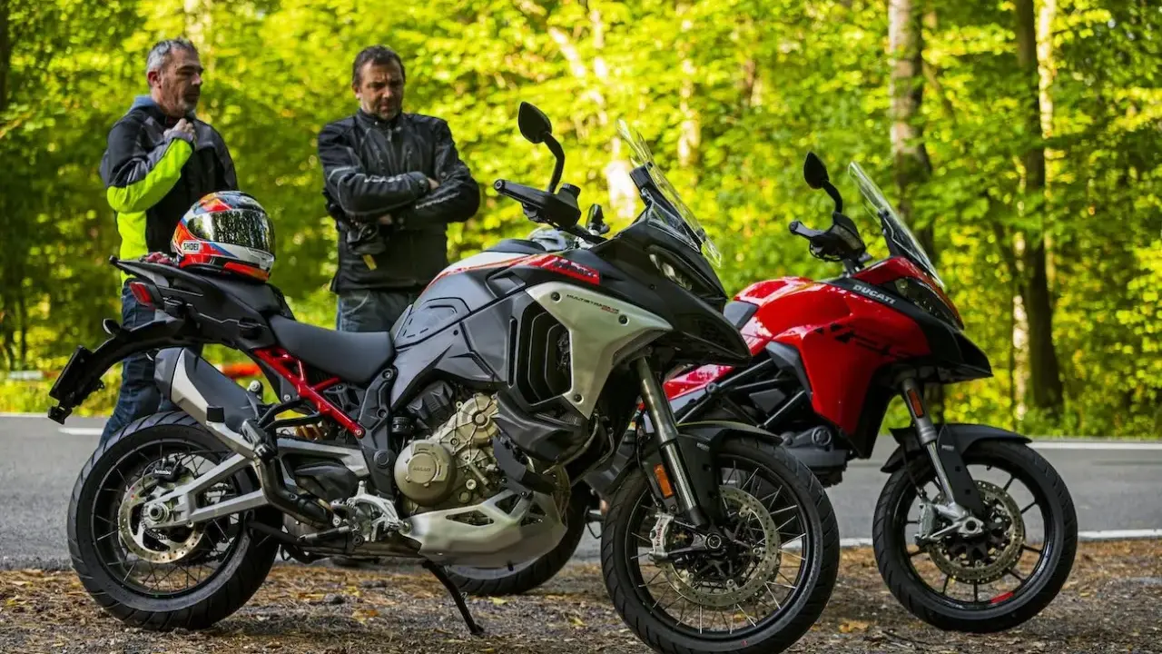 Dwóch motocyklistów przy dwóch motocyklach Ducati Multistrada V2, jeden szary, drugi czerwony, na tle leśnej drogi.