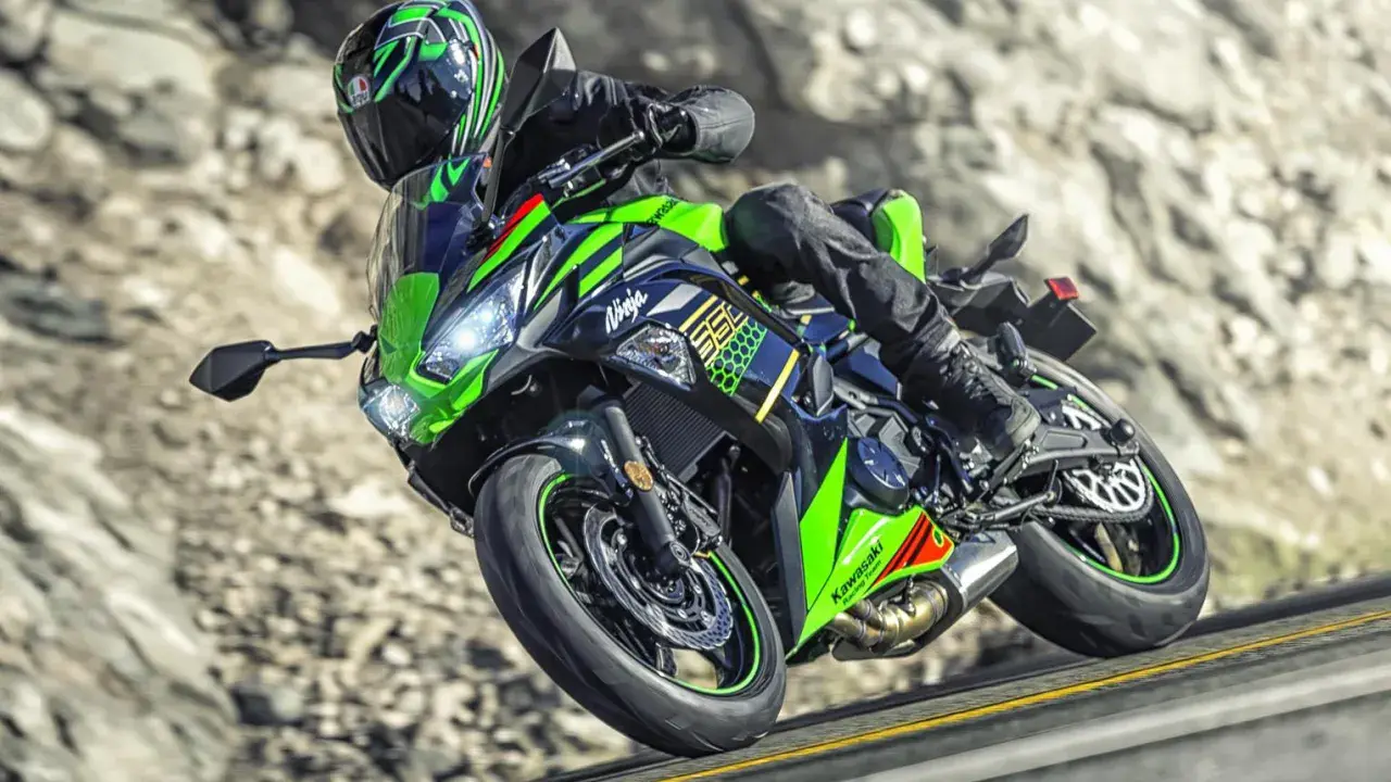 Motocyklista na zielono-czarnym Kawasaki Ninja 650, z widocznymi danymi technicznymi, pokonuje zakręt na górskiej drodze.
