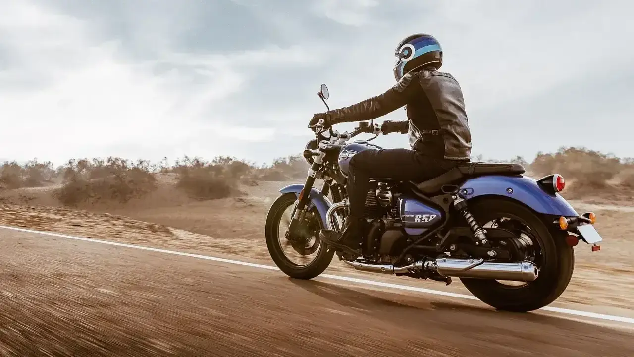 Motocyklista w skórzanej kurtce pędzi na niebieskim **super meteor 650** przez pustynny krajobraz.