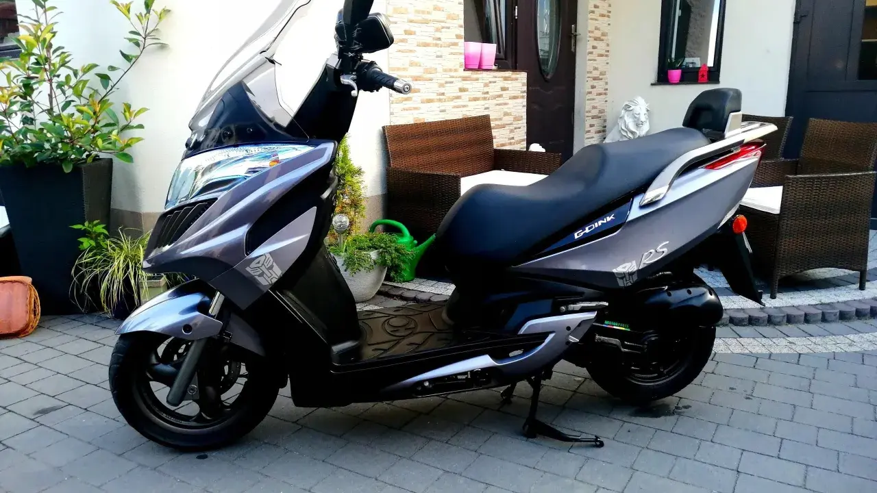 Elegancki skuter Kymco Dink 50 w kolorze grafitowym stoi na podjeździe, gotowy do jazdy.