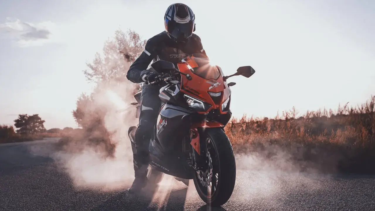 Motocyklista w kasku i kombinezonie na pomarańczowym Barton Blade 125, z którego unosi się dym. Zastanawiasz się, ile pali motor 125?