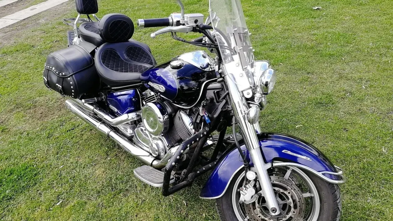 Błyszczący, niebieski motocykl Yamaha Drag Star 1100 z sakwami i dużą szybą, gotowy na podróż. Dane techniczne tego klasyka są imponujące.