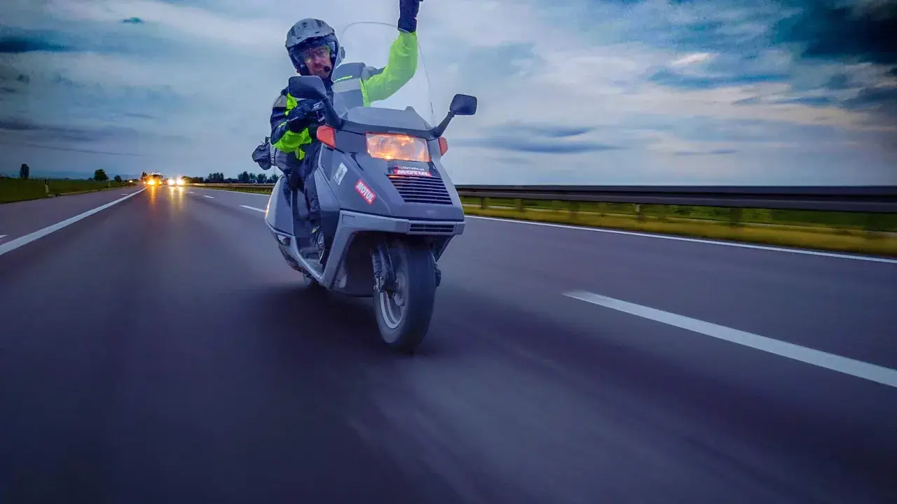 Motocyklista na skuterze 125 pozdrawia z autostrady, pokazując, że można nim jeździć po autostradzie.