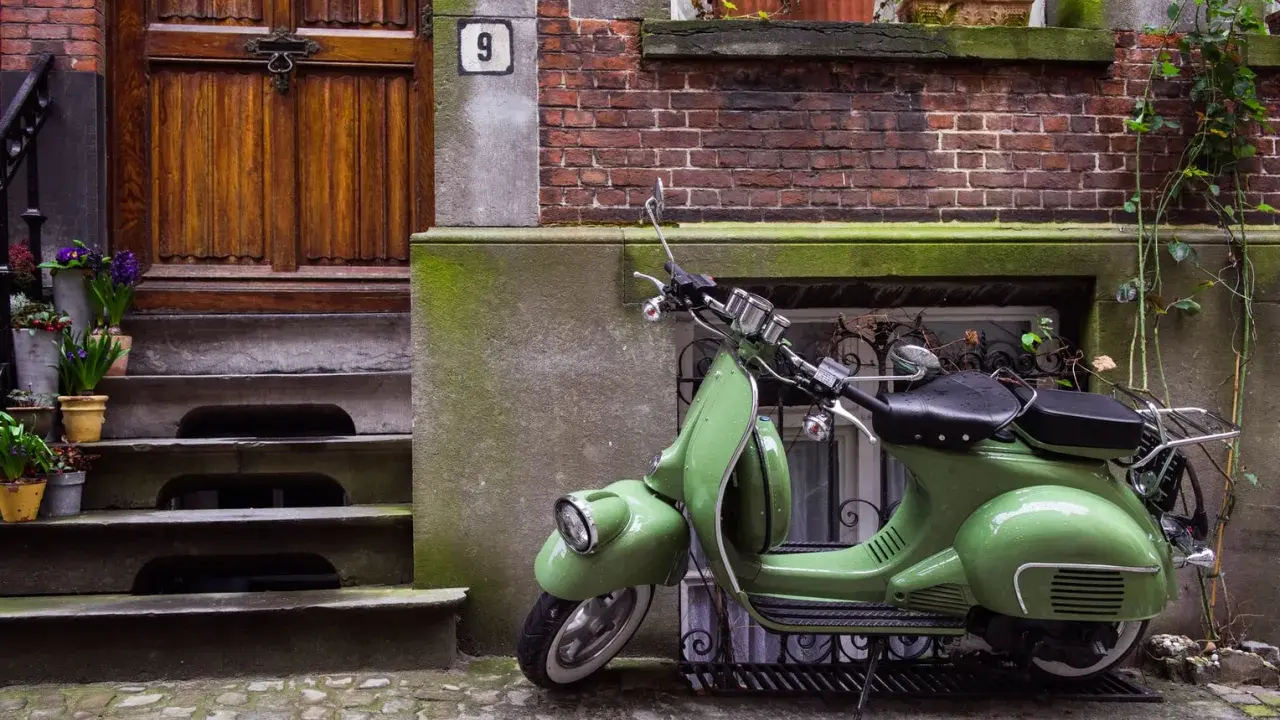 Zielony skuter, klasyk, czeka na właściciela. Parkowanie motocykla na chodniku przed drzwiami z numerem 9.