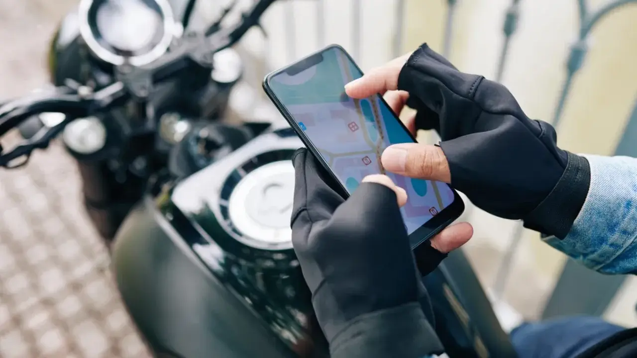 Motocyklista w rękawiczkach sprawdza trasę na mapie w aplikacji dla motocyklistów.