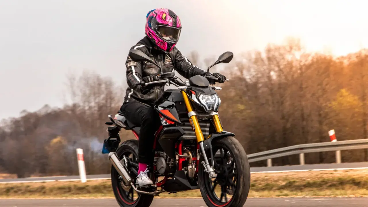 Motocyklistka w kolorowym kasku pędzi na czarnym motocyklu. Zastanawiasz się, ile waży litr benzyny, gdy tankujesz przed podróżą?
