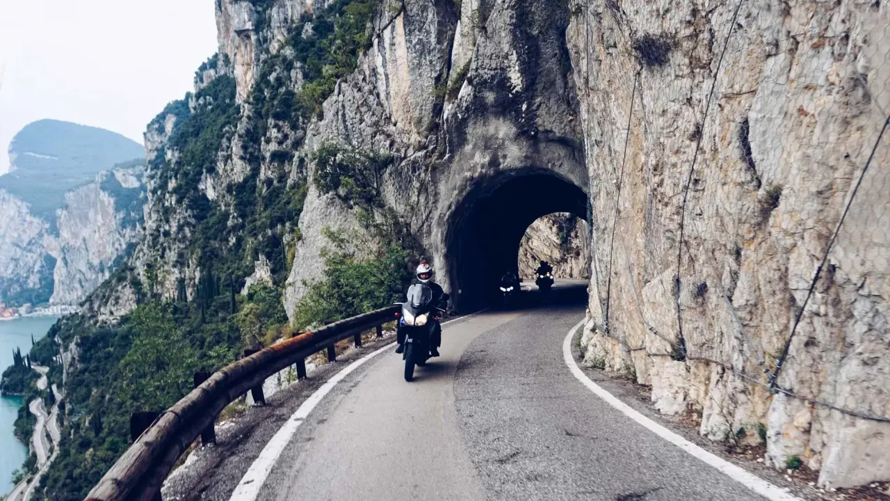 Motocykliści przemierzają malowniczą strada della forra, wjeżdżając w skalny tunel. Widok na jezioro i góry zapiera dech.