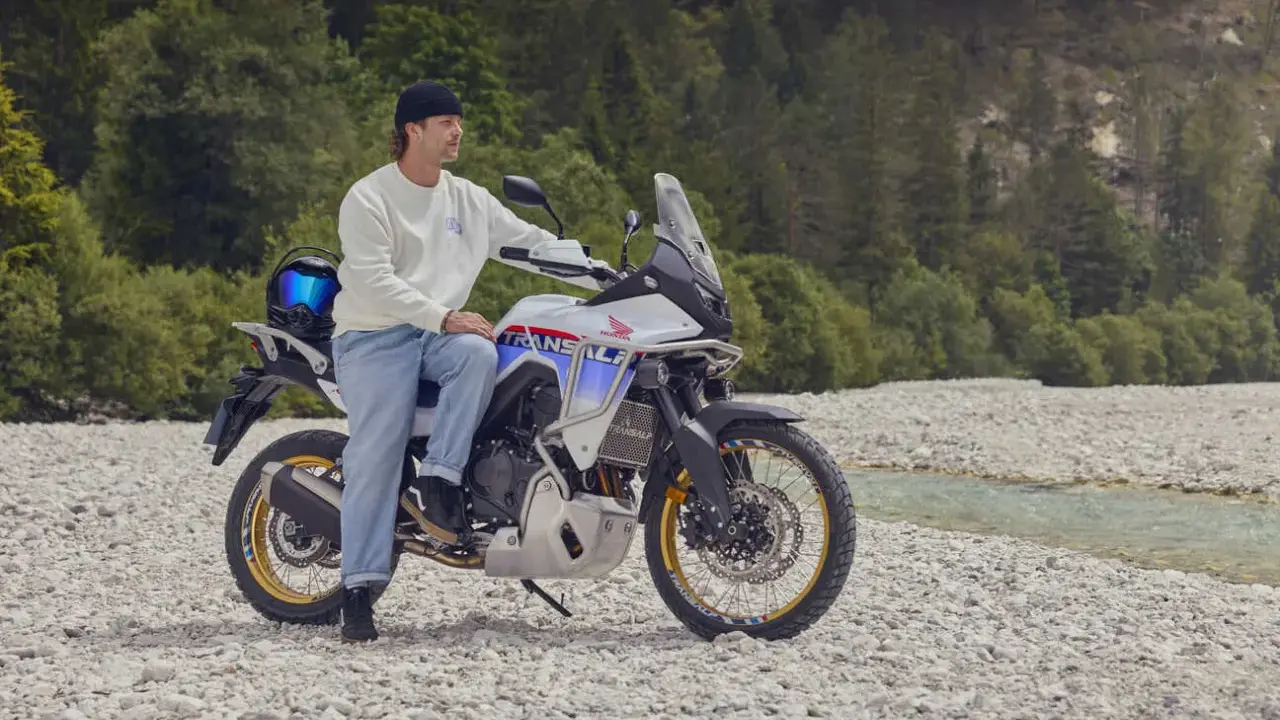 Mężczyzna na motocyklu Honda Transalp, gotowy na przygodę motocyklem po Europie. W tle las i strumień.