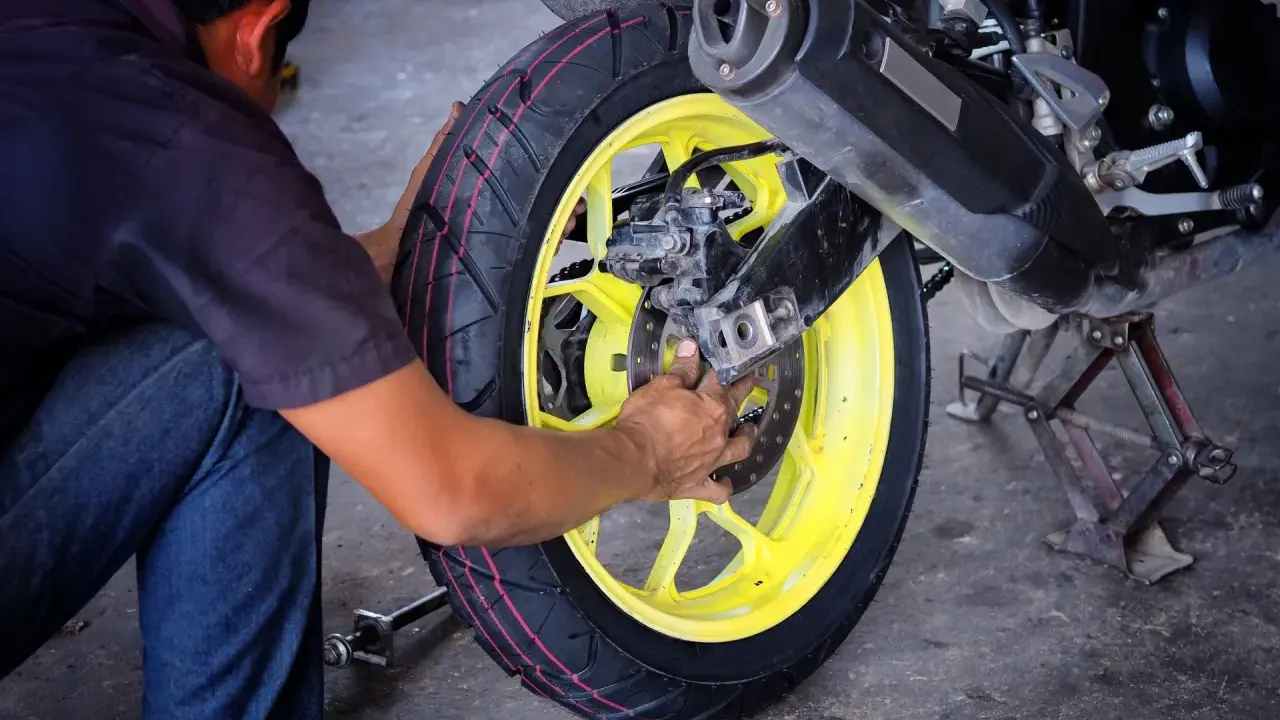 Mechanik dokonuje wymiany opon motocyklowych, pracując przy żółtej feldze i hamulcach.