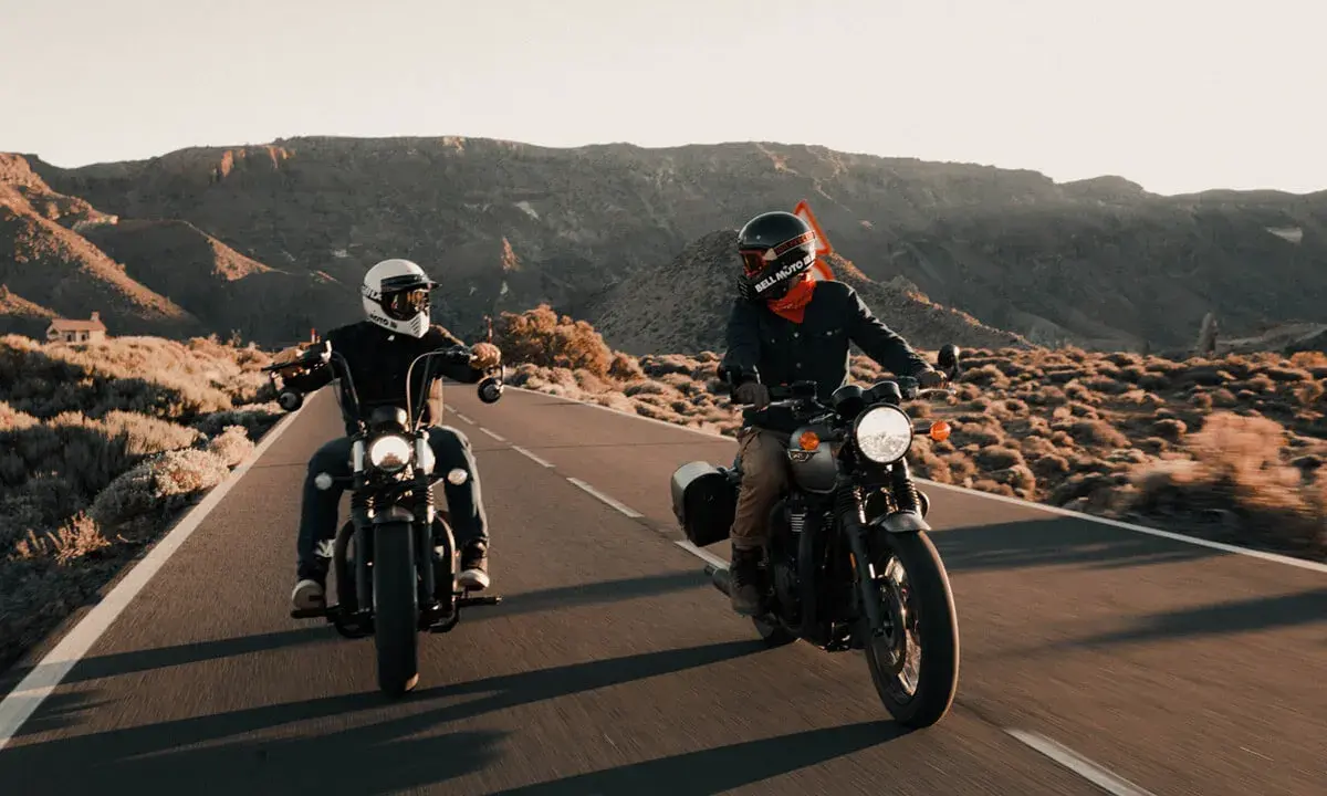 Dwóch motocyklistów w stylowym ubraniu na motor turystyczny przemierza pustynną drogę.