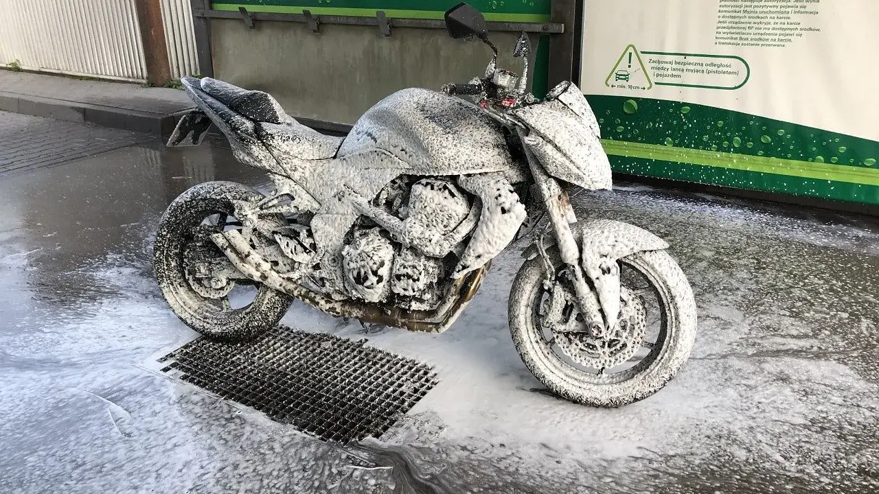 Motocykl pokryty pianą na myjni, gotowy do mycia. Instrukcja "jak myć motocykl" w tle.