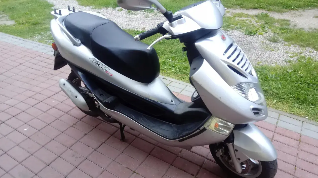 Srebrny skuter Kymco Bet&Win 50 stoi na chodniku z kostki brukowej.