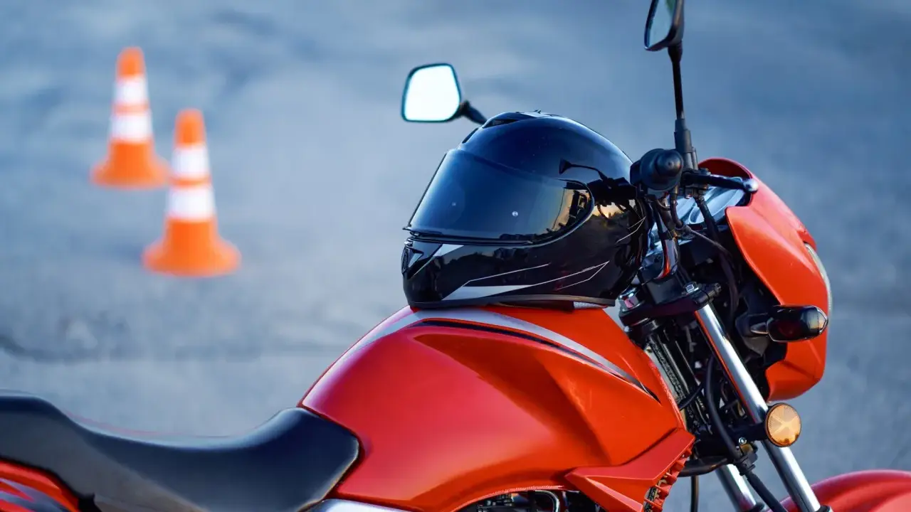 Pomarańczowy motocykl z kaskiem na baku i pachołkami w tle. Czy na motor trzeba mieć prawo jazdy? Tak, do prowadzenia motocykla wymagane jest odpowiednie prawo jazdy.