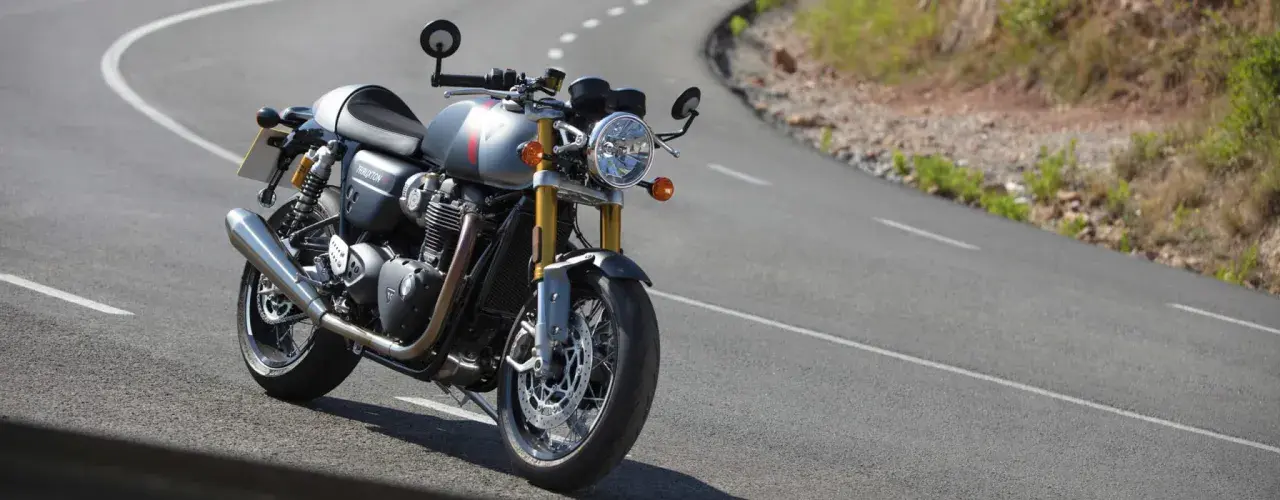 Srebrny Triumph Thruxton 900 na krętej drodze, gotowy na triumfalną jazdę.