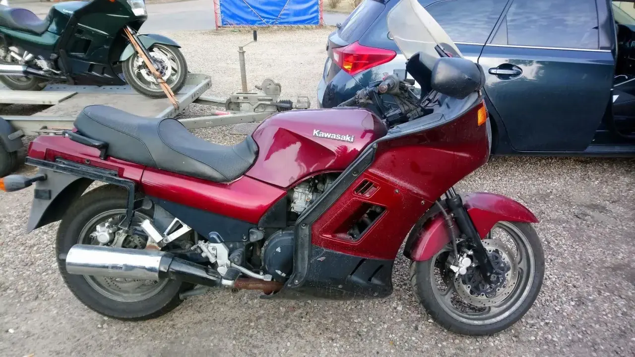 Czerwony motocykl Kawasaki GTR 1000 na przyczepce, obok ciemny samochód.