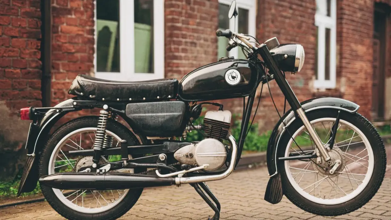 Czarny motocykl wsk 125 na tle ceglanego budynku. Klasyk z PRL-u gotowy do jazdy.