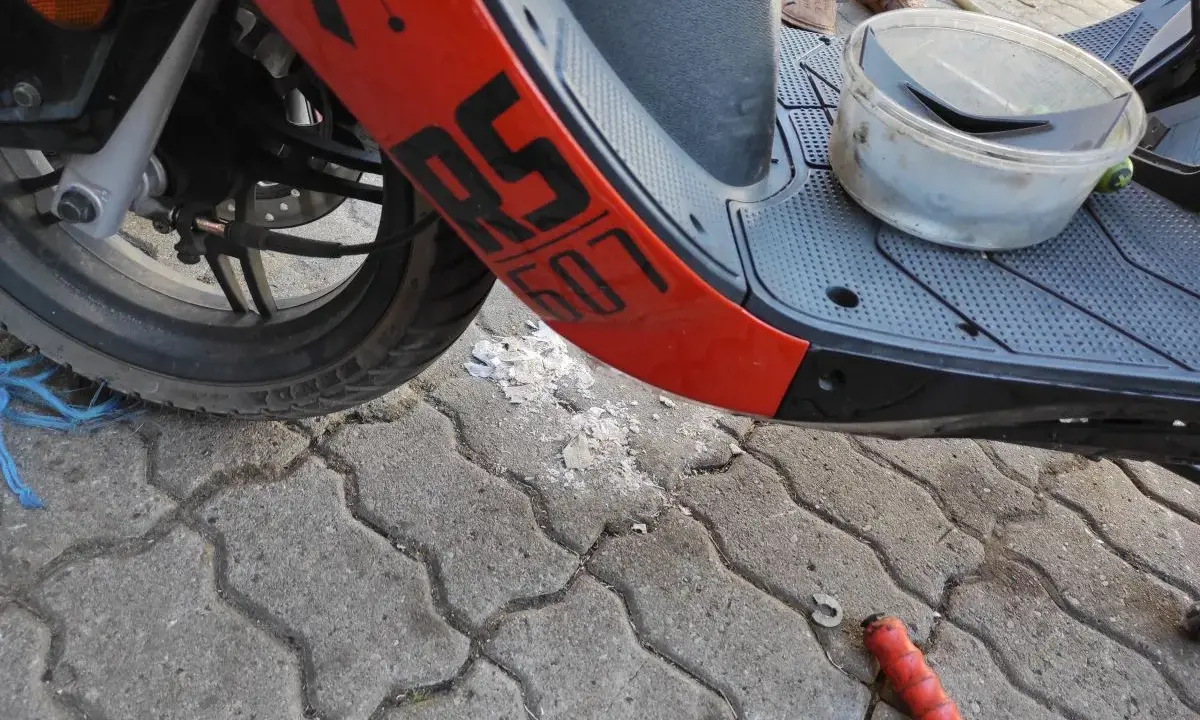 Część skutera Junak 607 4T z pomarańczowym elementem i napisem "607". Na podłodze leżą części i pojemnik.