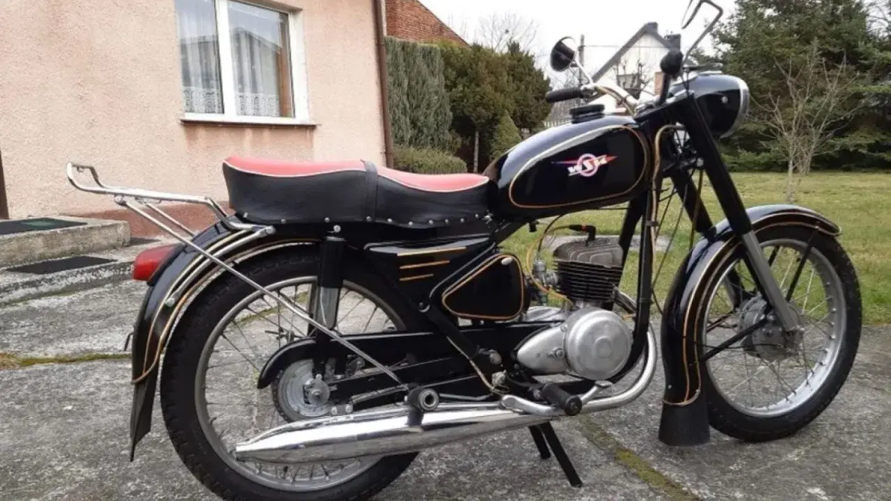 Czarny motocykl z PRL-u, z czerwonym siedzeniem i złotymi ozdobami. Klasyka polskich motocykli.