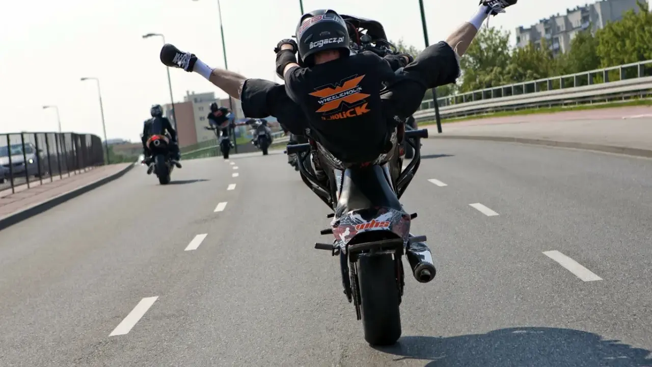 Motocyklista wykonuje jazdę na jednym kole z nogami w powietrzu. Ryzykowne wyczyny mogą skończyć się mandatem.