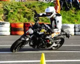 Motocyklista w kombinezonie i kasku wykonuje zakręt, przyjmując sportową pozycję na motocyklu.