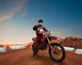 Motocyklista w kasku i stroju gotowy do jazdy po pustynnym torze. Idealne miejsce, gdzie można jeździć crossem, z klifami w tle.