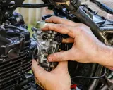 Dłonie mechanika regulują gaźnik motocykla, gdy ssanie jest włączone.