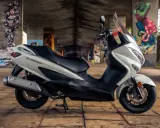 Biały skuter Suzuki Burgman 125, z czarnym siedzeniem, zaparkowany pod mostem z graffiti. Poznaj suzuki burgman 125 dane techniczne.