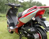 Czerwony skuter 50cc na trawie. Zastanawiasz się, ile jedzie skuter 50 bez blokad? Ten model wygląda na gotowy do szybkiej jazdy!