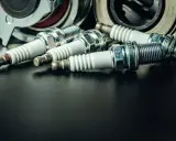 Kilka czarnych świec zapłonowych leży obok metalowych części.