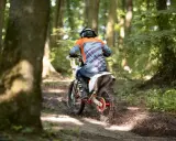 Motocyklista w kasku i pomarańczowej bluzie pędzi leśnym szlakiem. Od ilu lat można jeździć crossem? Odpowiedź zależy od przepisów i umiejętności.