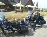 Motocyklista w skórzanej kurtce i spodniach odpoczywa przy swoim motocyklu. W tle karczma "Bida", idealne miejsce na postój podczas odkrywania **tras motocyklowych lubelskich**.