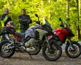 Dwóch motocyklistów przy dwóch motocyklach Ducati Multistrada V2, jeden szary, drugi czerwony, na tle leśnej drogi.