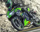 Motocyklista na zielono-czarnym Kawasaki Ninja 650, z widocznymi danymi technicznymi, pokonuje zakręt na górskiej drodze.