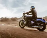 Motocyklista w skórzanej kurtce pędzi na niebieskim **super meteor 650** przez pustynny krajobraz.