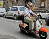 Mężczyzna w kasku jedzie skuterem elektrycznym, przygotowując się do testu na kartę motorowerową.