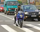 Motocyklista w kasku i kombinezonie na pasach. Obok samochody i furgonetka. Pamiętaj o przeglądzie, bo jaka kara za brak przeglądu może być dotkliwa.
