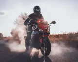 Motocyklista w kasku i kombinezonie na pomarańczowym Barton Blade 125, z którego unosi się dym. Zastanawiasz się, ile pali motor 125?