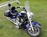 Błyszczący, niebieski motocykl Yamaha Drag Star 1100 z sakwami i dużą szybą, gotowy na podróż. Dane techniczne tego klasyka są imponujące.