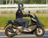 Pierwsze kroki w nauce jazdy na motorze 125. Kierowca w kasku i kurtce jedzie na skuterze Keeway po drodze.