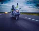 Motocyklista na skuterze 125 pozdrawia z autostrady, pokazując, że można nim jeździć po autostradzie.