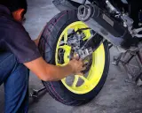 Mechanik dokonuje wymiany opon motocyklowych, pracując przy żółtej feldze i hamulcach.