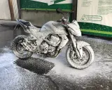 Motocykl pokryty pianą na myjni, gotowy do mycia. Instrukcja "jak myć motocykl" w tle.